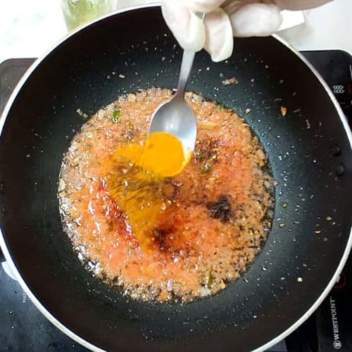 Raw egg being added to browned daal mash mixture in a dark wok with spoon.