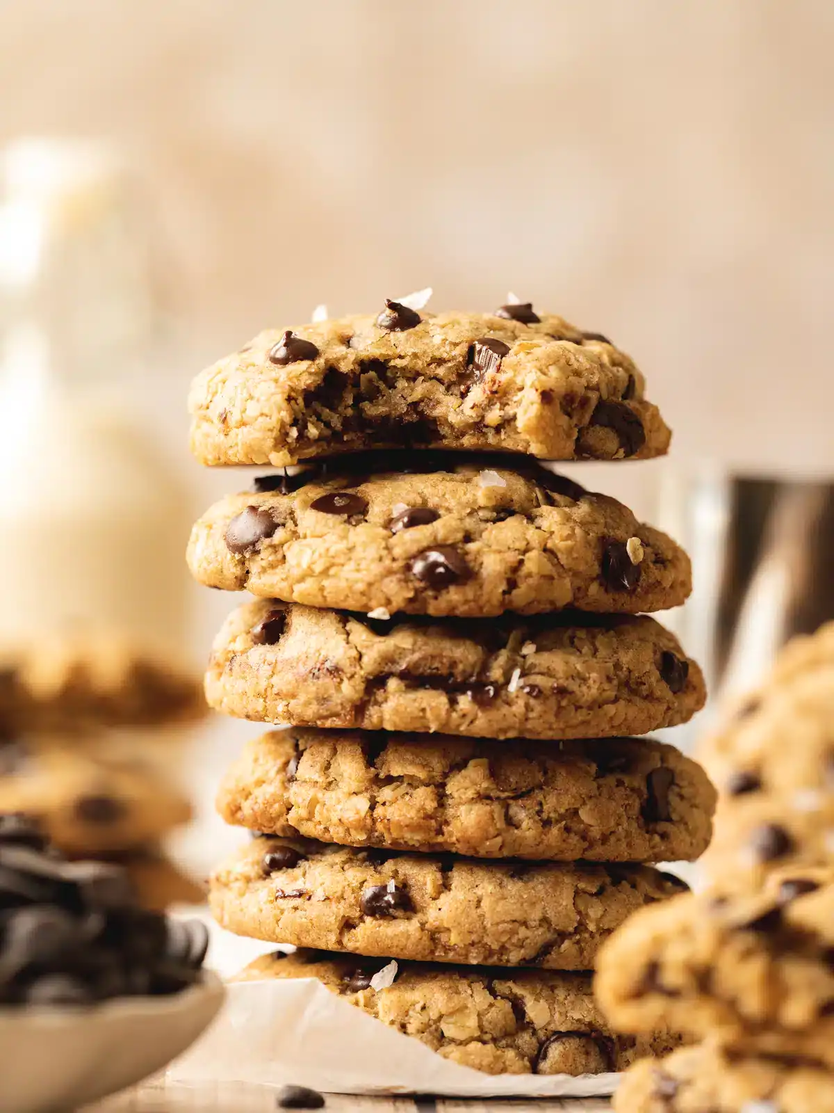 Stack of chocolate chip cookies with sea salt garnish on parchment paper.