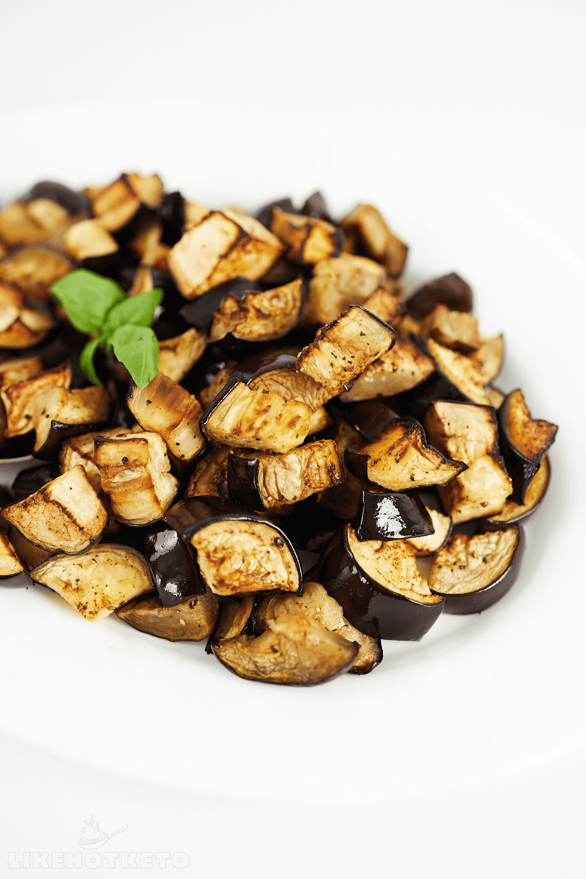 Roasted eggplant and potato chunks with golden-brown edges and fresh basil garnish on white plate.