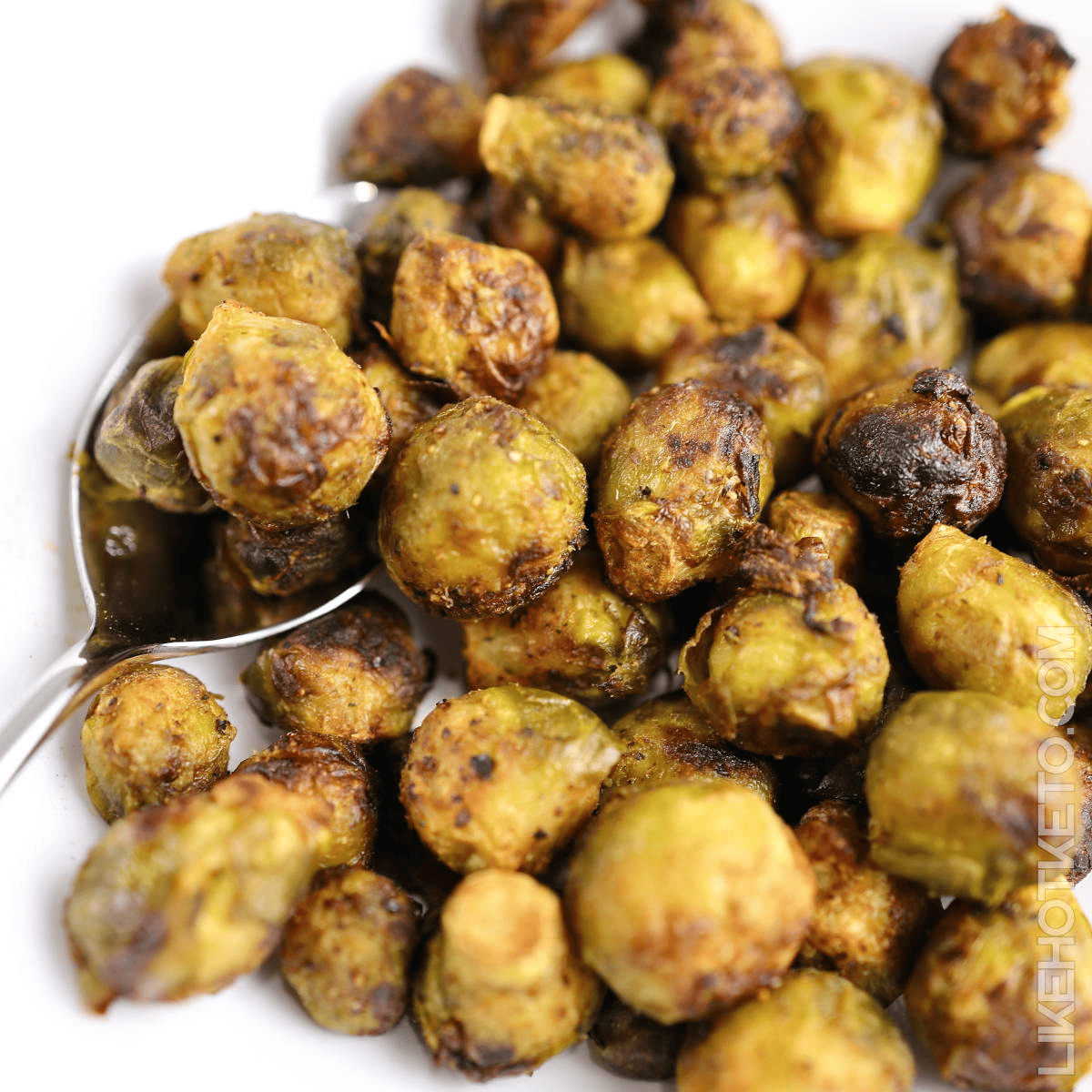 Roasted Brussels sprouts with golden-brown crispy exterior on white plate with serving spoon.