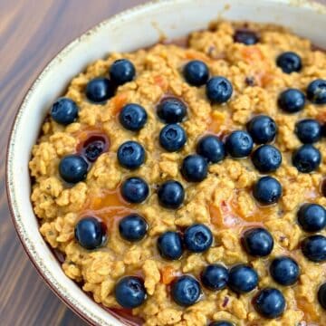 Blueberry baked oatmeal in white bowl with fresh blueberries and apricots scattered on top.
