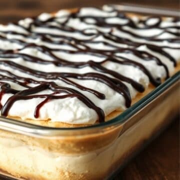 Cream puff cake in glass baking dish topped with whipped cream and chocolate drizzle.
