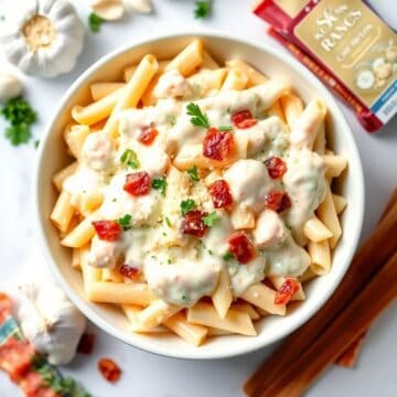 Creamy chicken bacon ranch pasta with crispy fries, fresh parsley, and red pepper garnish in white bowl.