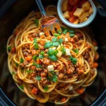 Crockpot taco spaghetti garnished with cilantro and diced onions in a dark bowl with a fork.