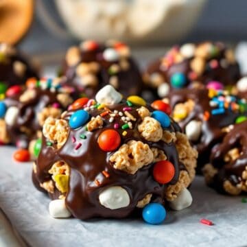 Colorful no-bake chocolate clusters topped with cereal, candy pearls, and sprinkles on gray surface.