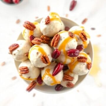 Mini cranberry pecan goat cheese balls drizzled with honey, garnished with nuts and cranberries on a white plate.