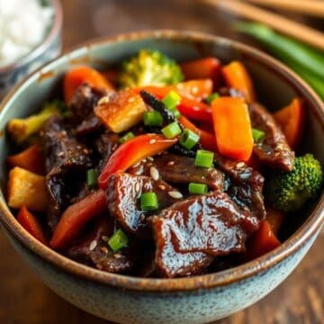 Teriyaki glazed beef stir-fry with broccoli, peppers, and sesame seeds in ceramic bowl.