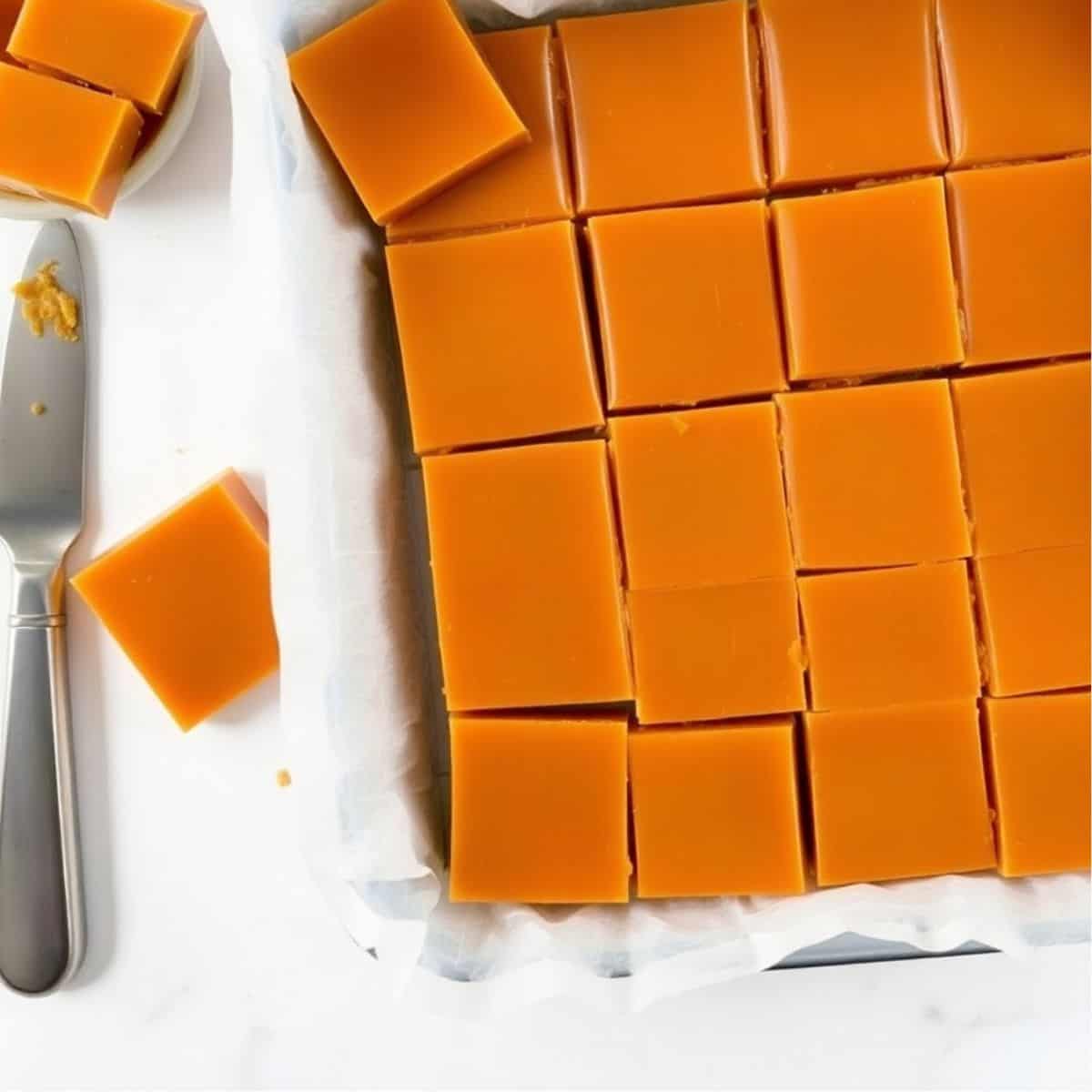 Golden-brown caramels cut into squares on parchment paper with a knife nearby.