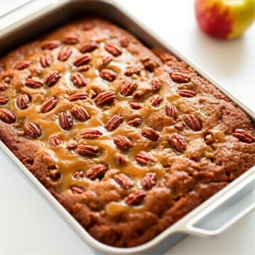 Apple pecan cake with caramel glaze in white baking dish, topped with pecans and caramel drizzle.