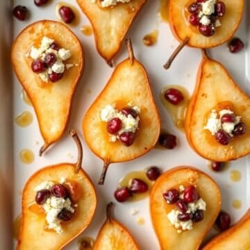 Baked pears halved and topped with crumbled feta cheese, red cranberries, and honey drizzle on white plate.