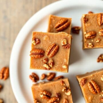 Butter pecan fudge squares topped with pecans arranged on a white plate.