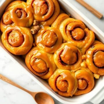 Caramel apple cinnamon rolls with glossy caramel glaze in a white ceramic baking dish.