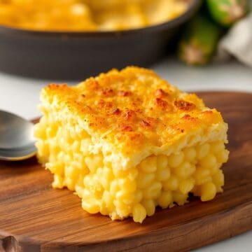 Golden-brown baked cheesy corn casserole squares with crispy tops on wooden serving board.