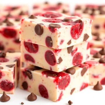 Stacked Cherry Garcia fudge squares with white chocolate, red cherries, and chocolate chips on white surface.