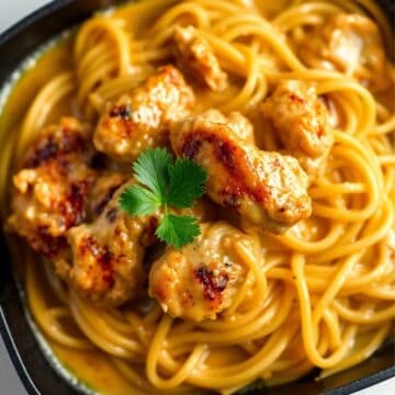 Seared chicken pieces with golden buttered noodles, garnished with fresh cilantro in a dark bowl.