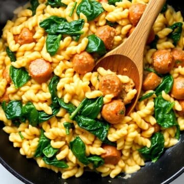 Creamy chicken sausage orzo skillet with golden pasta, sliced sausage, and fresh spinach in a dark pan.