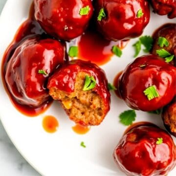Glossy cranberry meatballs with golden centers garnished with cilantro on a white plate.