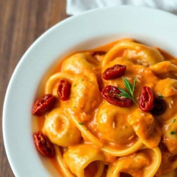 Marry Me Chicken Tortellini in creamy orange sauce, garnished with red chili peppers and fresh rosemary in white bowl.