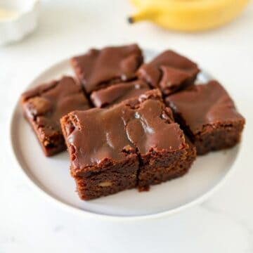 Banana bread brownies cut into squares on a white plate with chocolate frosting.