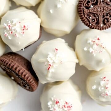White chocolate-coated peppermint Oreo balls garnished with crushed candy canes and chocolate cookies.