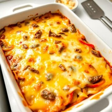Philly Cheesesteak Casserole with melted cheese, ground beef, and peppers in white baking dish.