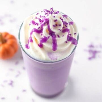 Purple Halloween Frappuccino in tall glass topped with whipped cream and purple sprinkles.