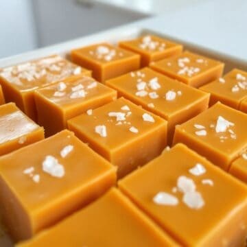 Homemade salted butterscotch fudge squares topped with sea salt flakes on parchment paper.