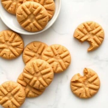 Soft peanut butter cookies with crosshatch pattern on white marble surface and plate.