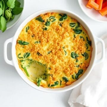 Golden-baked spinach and cheese casserole in white dish, garnished with fresh herbs.