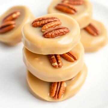 Stacked vanilla pecan pralines with whole pecans on white surface, creamy caramel coating.