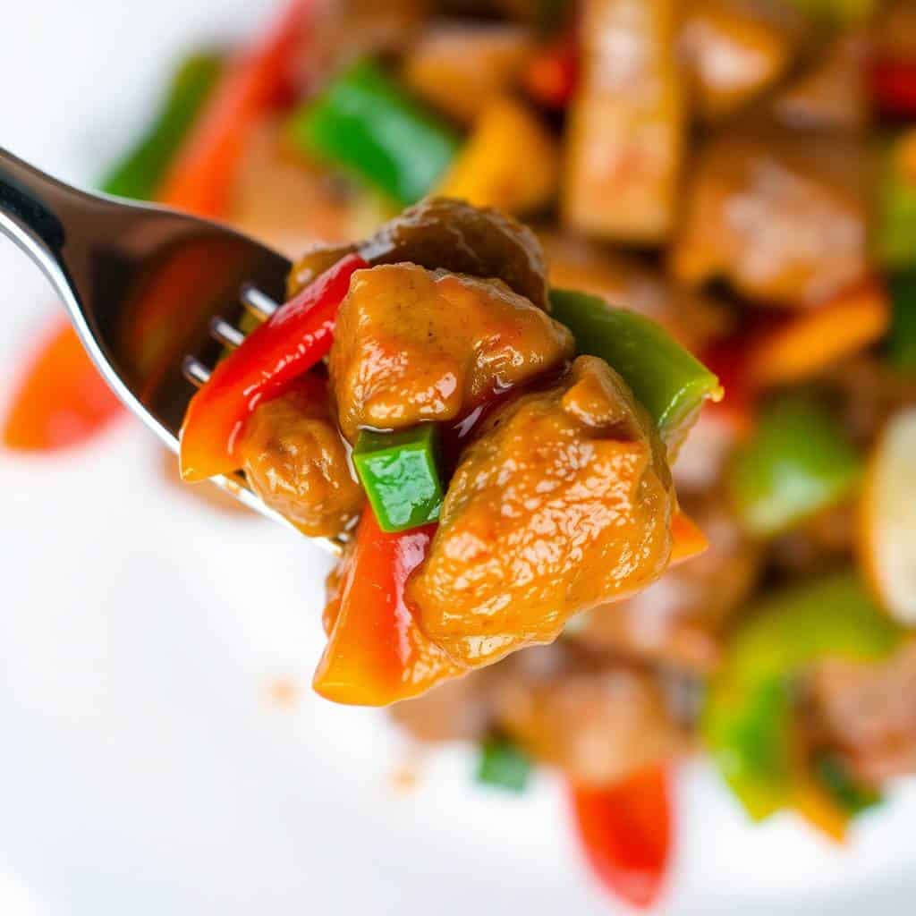 Beef stir-fry with bell peppers on fork, garnished with green onions, served on white plate.