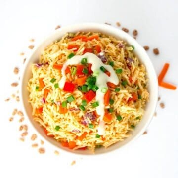 Colorful creamy orzo salad with vegetables and dressing in a white bowl.