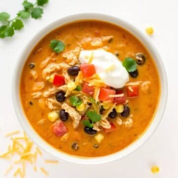 Enchilada soup with chicken, cheese, black beans, and fresh toppings in a white bowl.