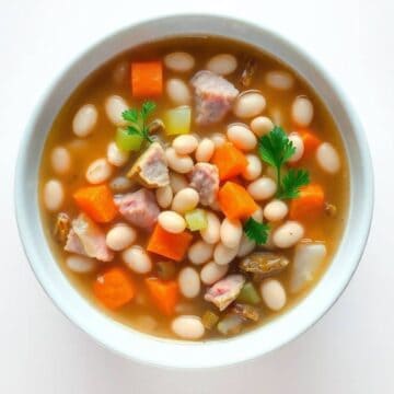 Hearty ham and bean soup with vegetables in a white bowl.