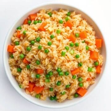 Homemade fried rice with peas and carrots in a white bowl.