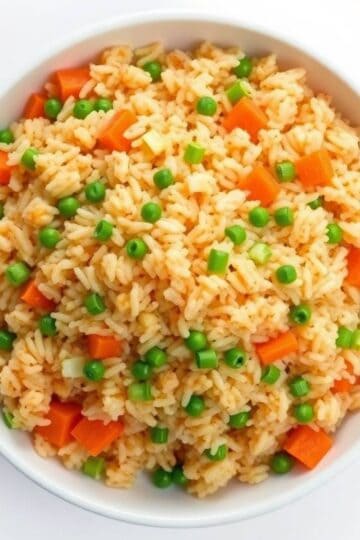 Homemade fried rice with peas and carrots in a white bowl.