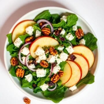 Fresh Honeycrisp apple slices with feta cheese, walnuts, and red onions on a bed of mixed greens.