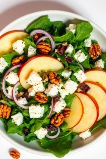 Fresh Honeycrisp apple slices with feta cheese, walnuts, and red onions on a bed of mixed greens.