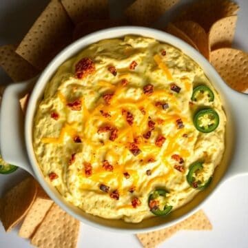 Delicious baked jalapeño popper dip topped with cheddar cheese, bacon bits, and sliced jalapeños, pe.