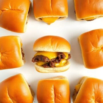 Close-up of beef sliders with cheddar cheese on soft buns, arranged on a white background.