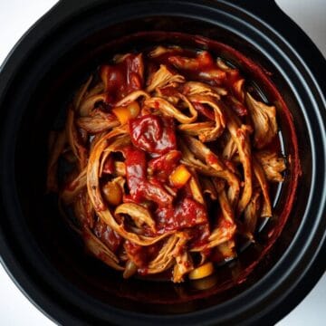 Slow cooker pulled pork with barbecue sauce and vegetables in a black crockpot.