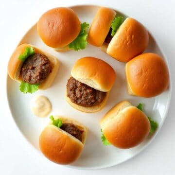 Mini beef sliders with lettuce on a white plate, perfect for appetizers or snacks.