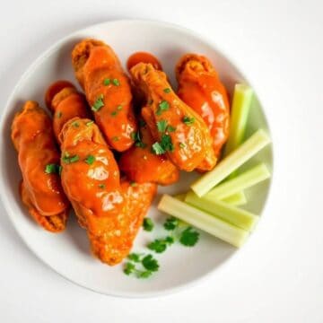 Buffalo chicken wings with hot sauce and fresh herbs on a white plate.