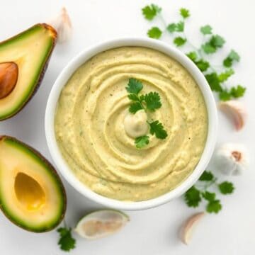 Avocado dip with cilantro in a white bowl, garnished with cilantro leaves.