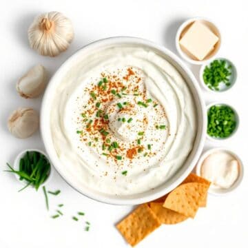 Ranch dip in a white bowl garnished with chopped green onions and paprika, served with garlic, chees.