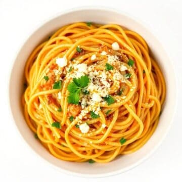 Cream cheese spaghetti with herbs and cheese in a white bowl.