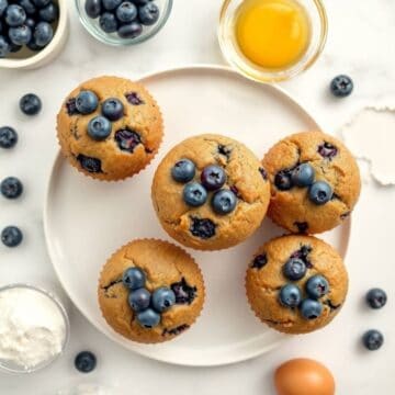 Delicious homemade blueberry muffins topped with fresh blueberries on a white plate.