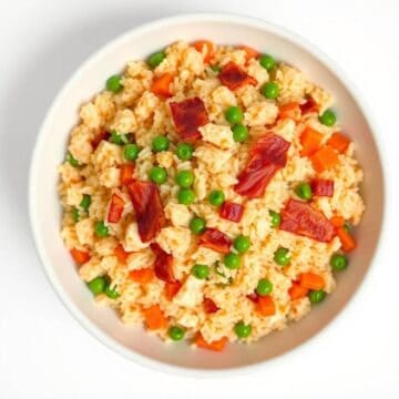 Delicious chicken and bacon fried rice with peas and carrots in a white bowl.