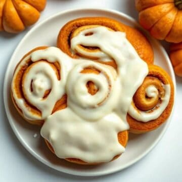 Delicious pumpkin cinnamon rolls with cream cheese frosting on a white plate.