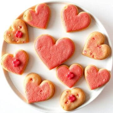 Heart-shaped cookies with pink icing and red decorations on a white plate.